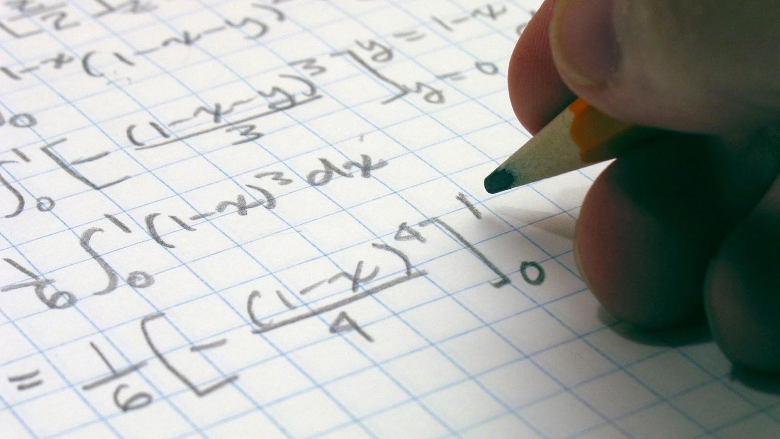 dłoń trzymająca ołówek zapisująca w zeszycie w kratkę równania różniczkowe i całkowe
