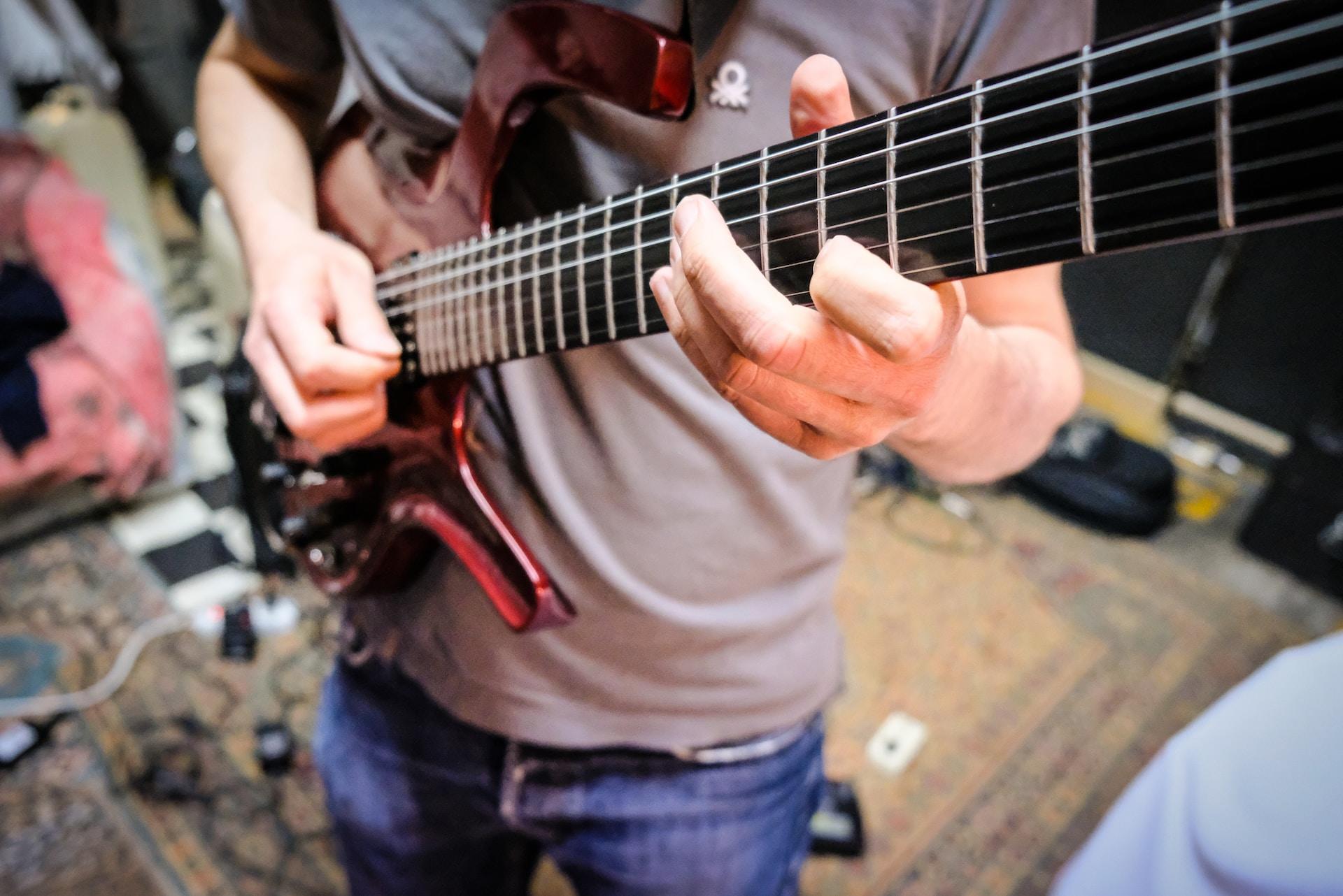 Mężczyzna w szarej koszulce grający na czerwonej gitarze elektrycznej.