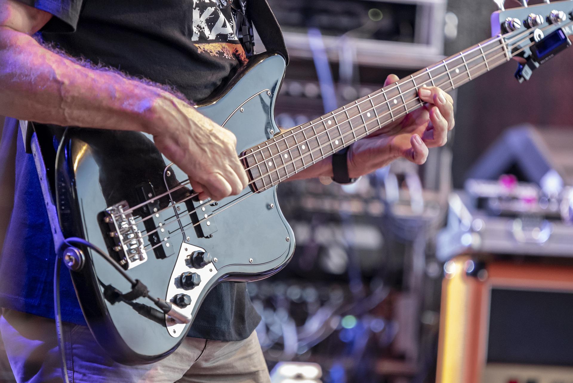 Mężczyzna grający na czarnej gitarze basowej na scenie.