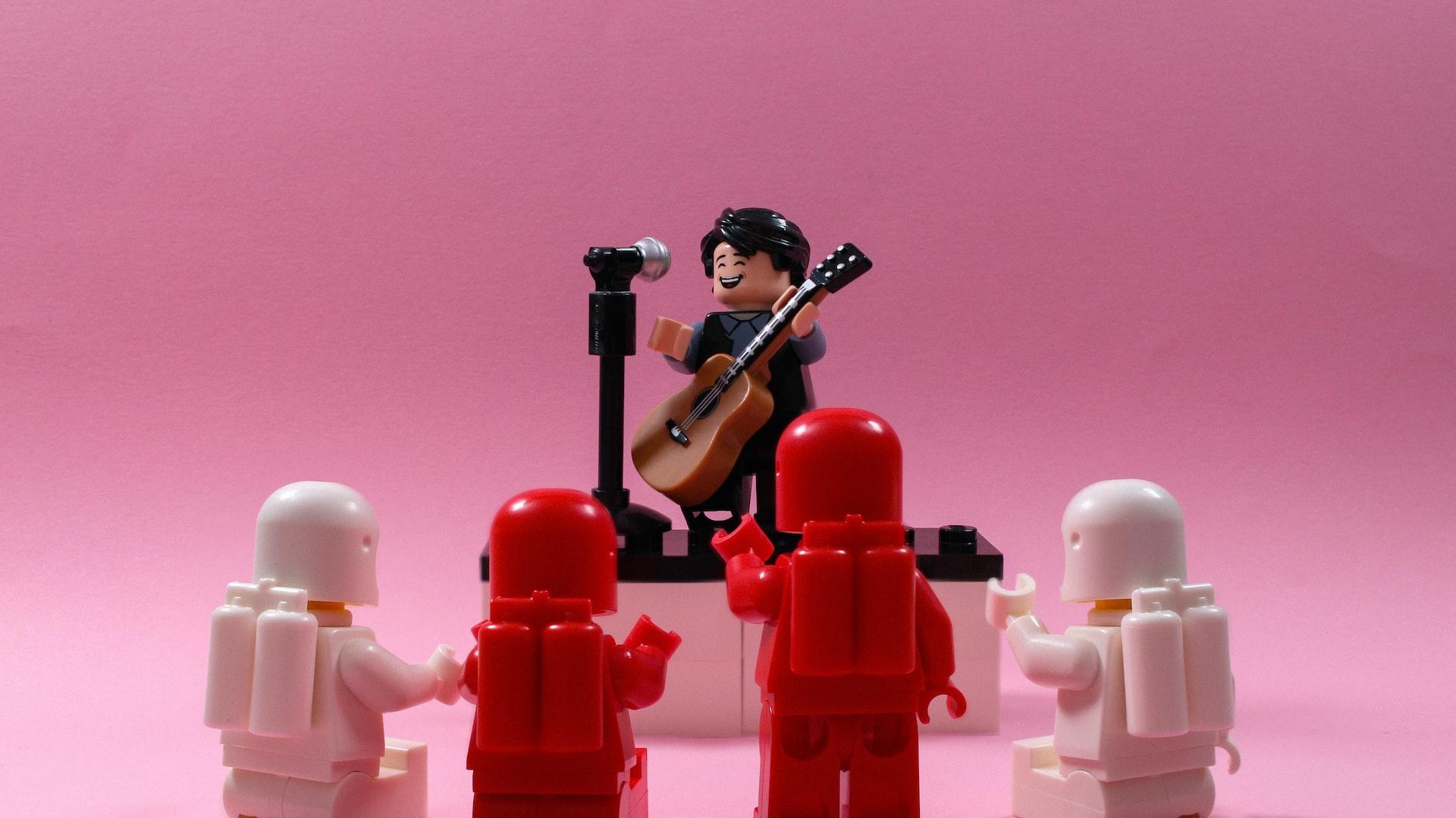 Klocki LEGO: ludziki, gitara i mikrofon na statywie na różowym tle.