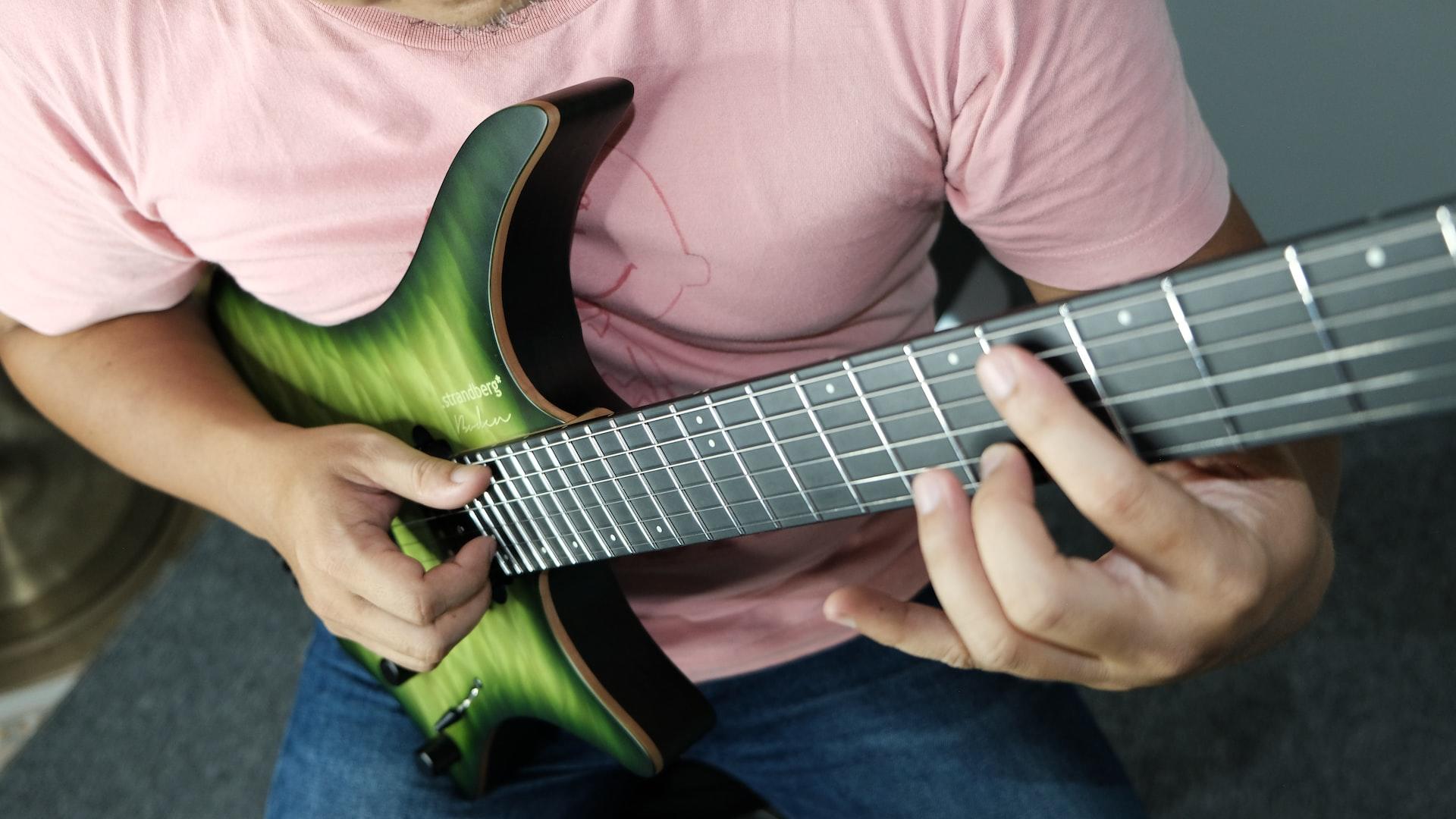 Mężczyzna w różowej koszulce grający na zielonej gitarze elektrycznej.