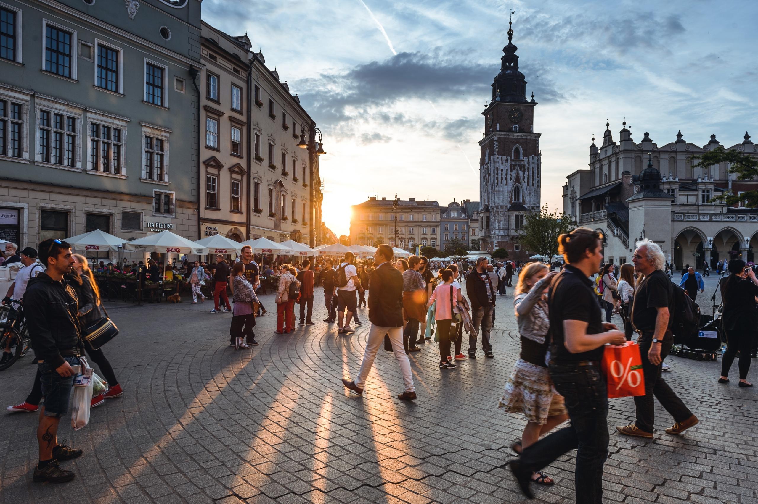 Rynek, centrum miasta oraz tłumy osób spacerujacych w tle zachodzącego słońca