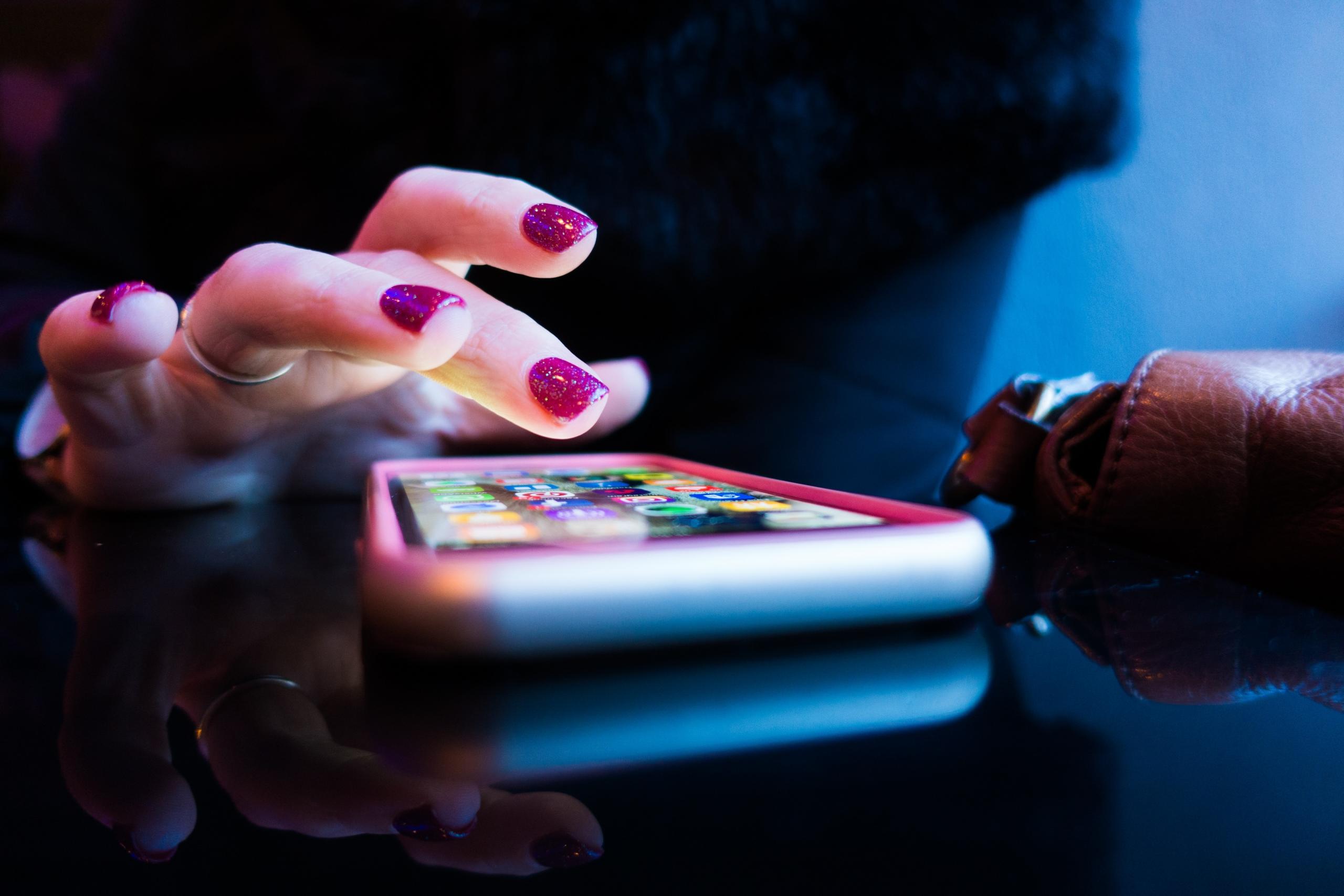 W przybliżeniu telefon, świecący ekran oraz dłoń kobiety