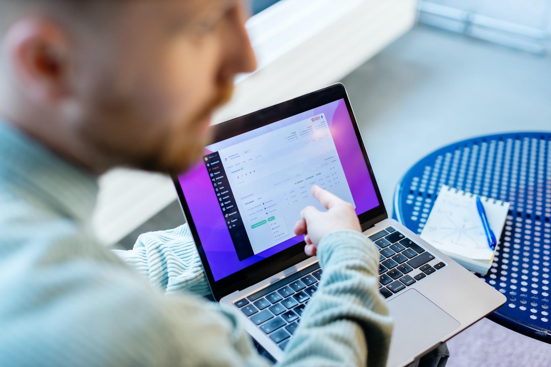 Mężczyzna wskazujący na otwarty laptop leżący na stoliku.