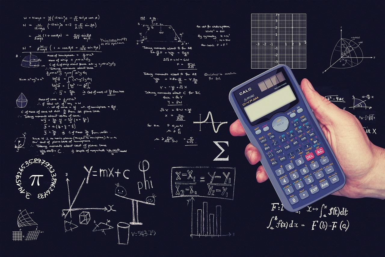 tablica ze wzorami matematycznymi oraz ręka trzymająca kalkulator