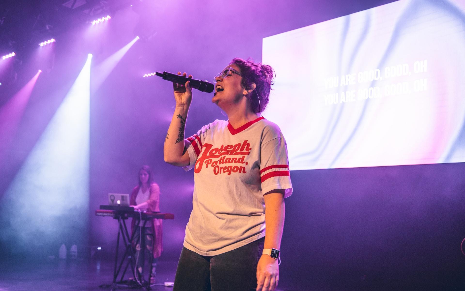 Kobieta z mikrofonem na scenie, karaoke, fioletowe oświetlenie.