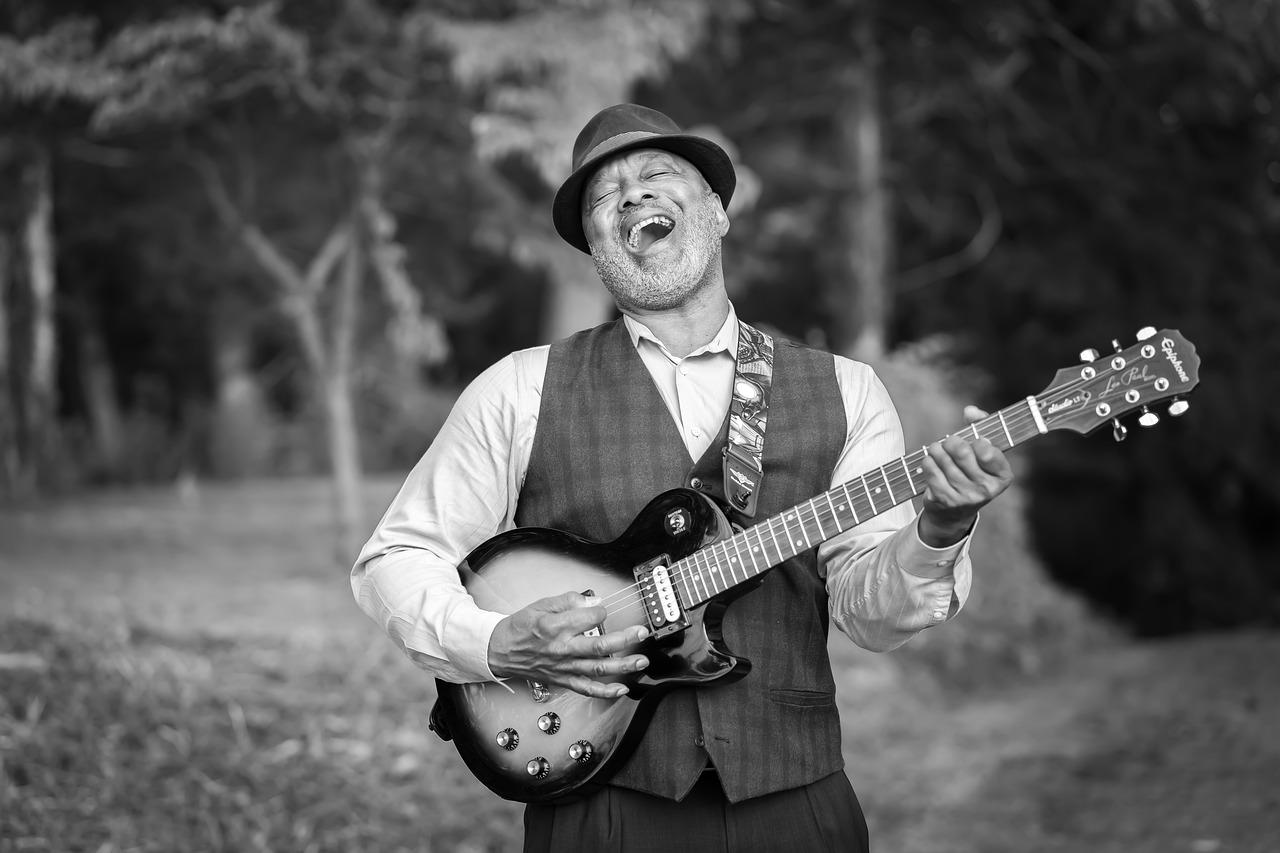 Czarno biały portret śpiewającego mężczyzny z gitarą, z tyłu drzewa i trawa