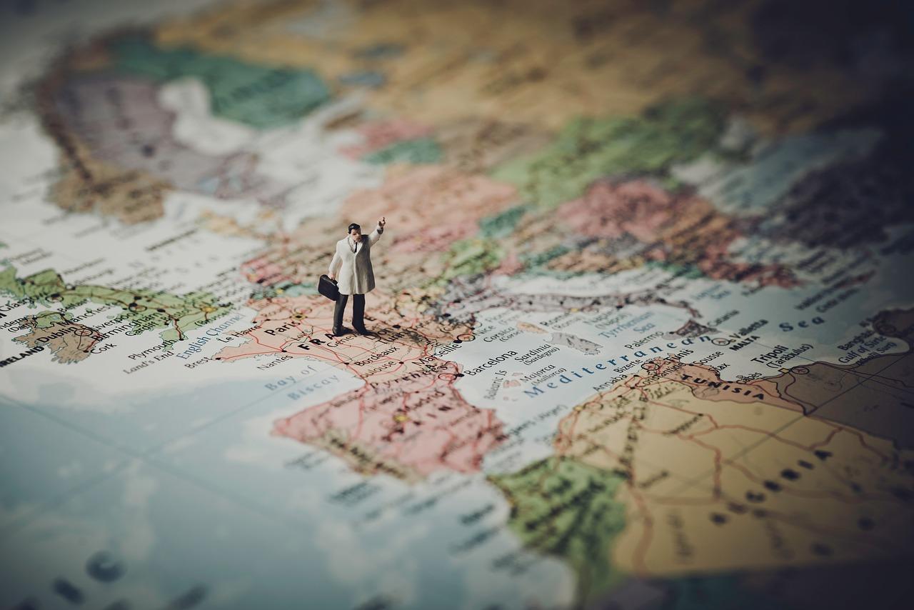 Figurka mężczyzny w białym płaszczu z teczką, z ręką w górze, stojąca na mapie, mapa Francji, mapa Europy.