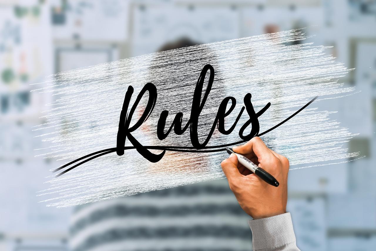 Dłoń z długopisem, napis rules na szybie, człowiek przy tablicy.