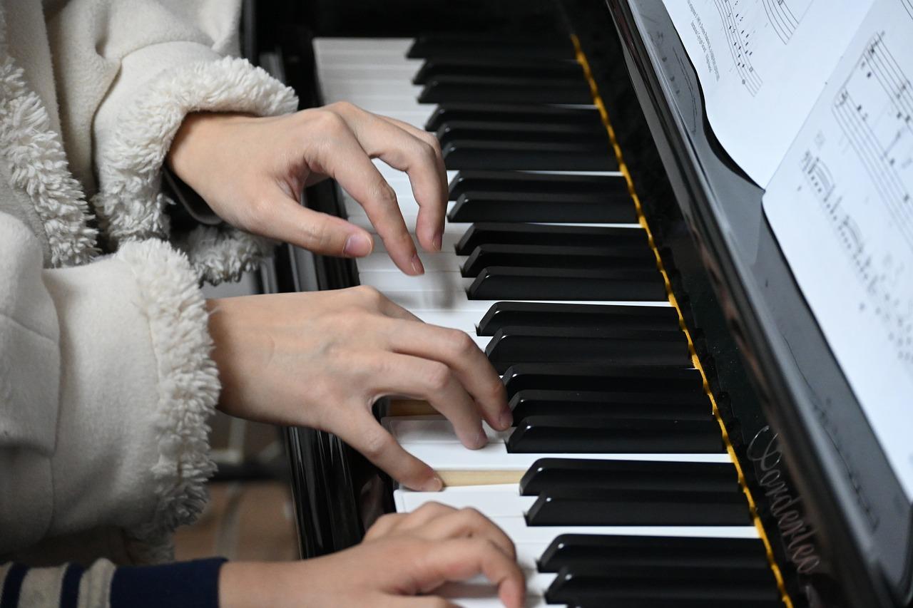 Ludzie przy pianinie, dłonie na klawiszach pianina, zapis nutowy, arkusz z nutami, lekcja gry na pianinie.