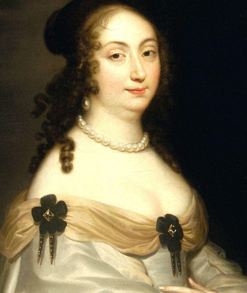 Portret kobiety w historycznej sukni z odkrytymi ramionami, ozdobionej czarnymi broszkami w kwiaty i naszyjnikiem z pereł.