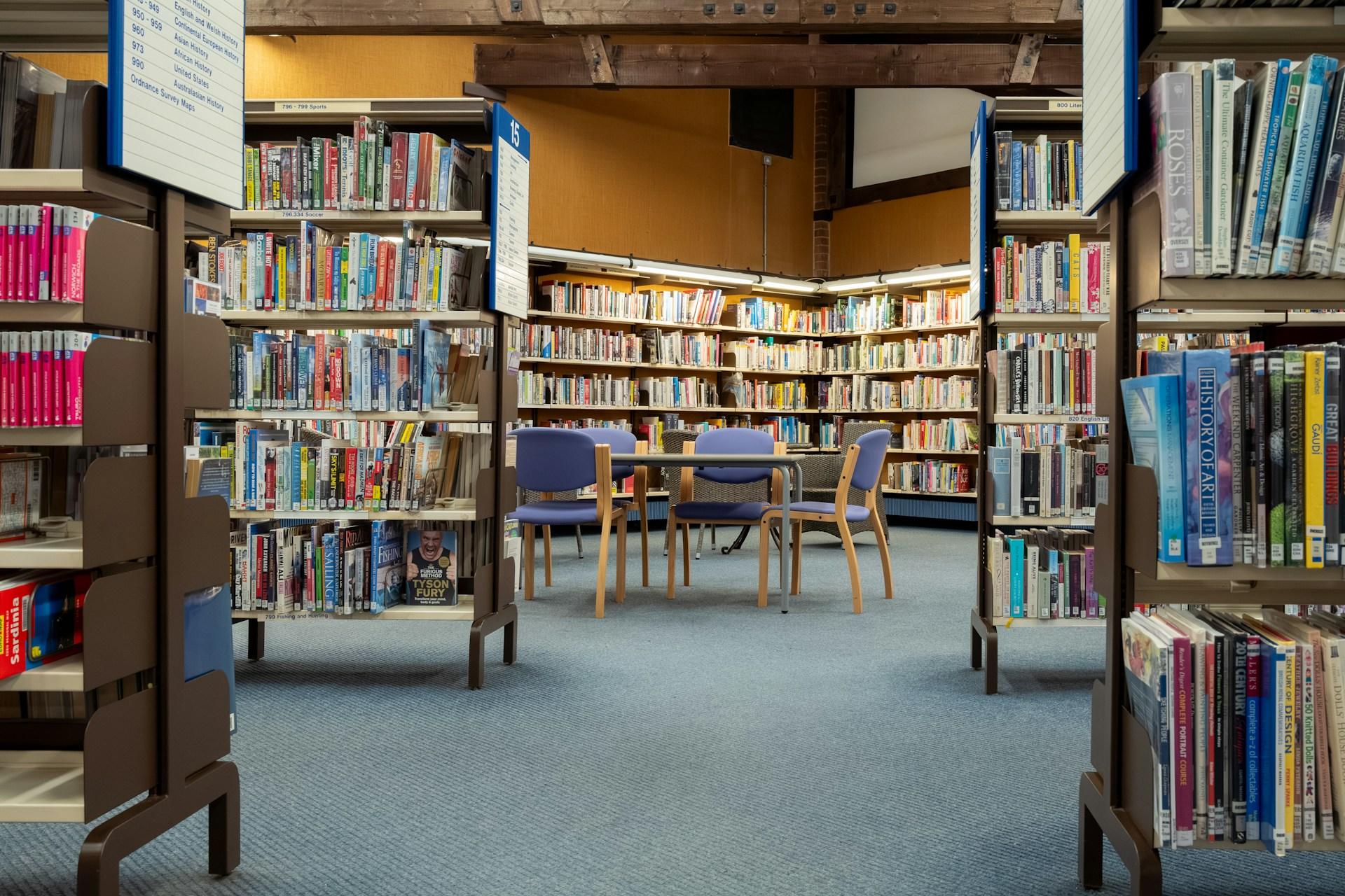 Biblioteka, książki na regałach, stolik z krzesłami.