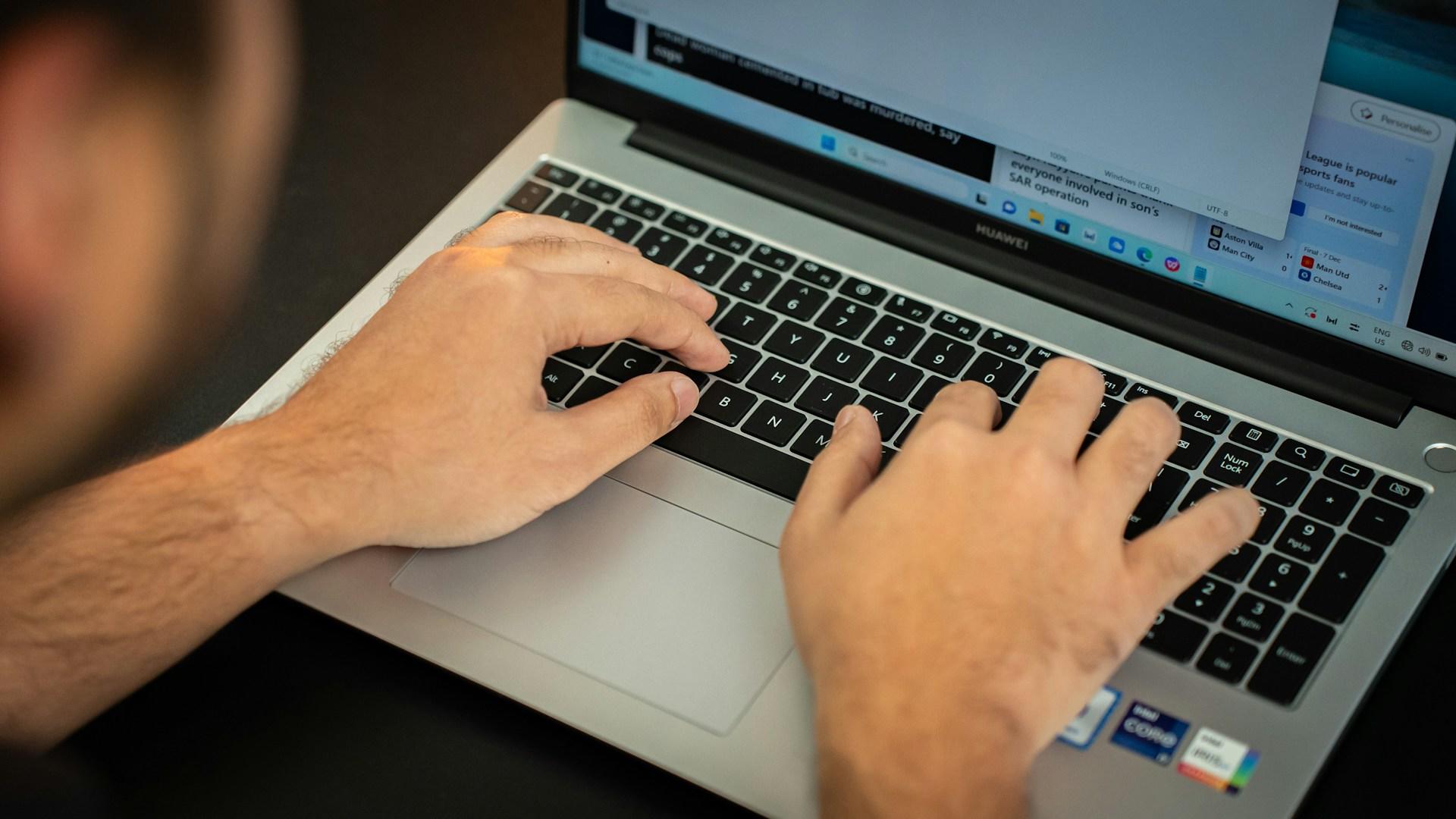 Dłonie mężczyzny na klawiaturze laptopa.
