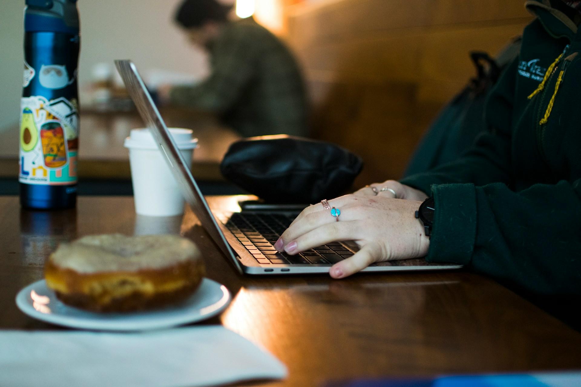 Dłonie na klawiaturze, laptop, kawiarnia.
