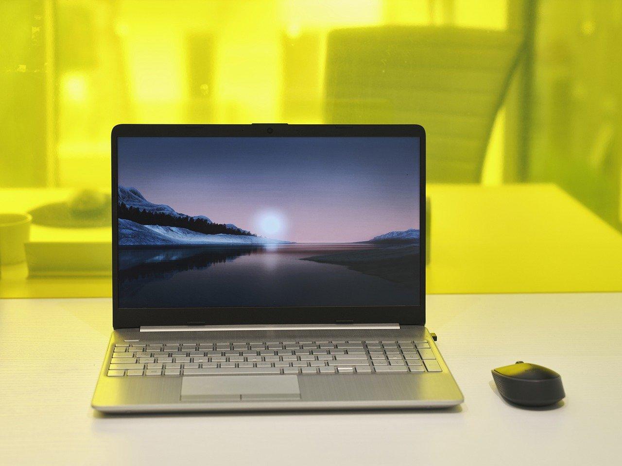 Laptop i myszka komputerowa na białym stole.