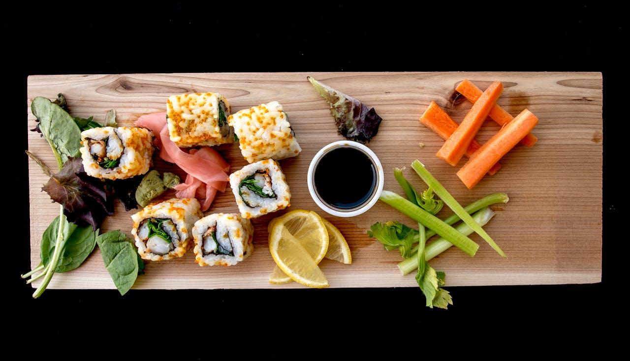 na drenianej desce serwowane sushi, warzywa i sos sojowy