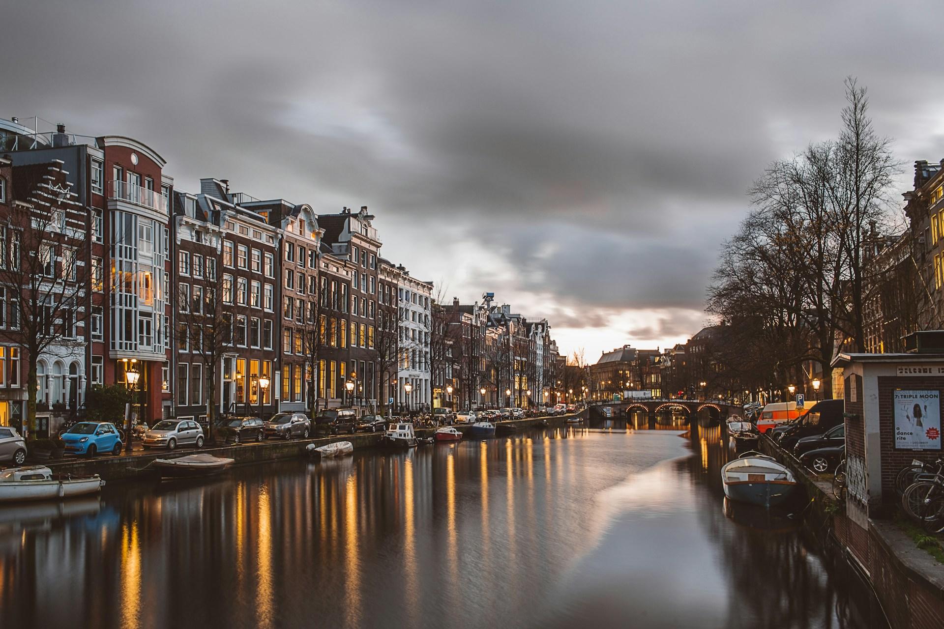 amsterdam, kanał, domki holenderskie, łodzie, samochodzy  wzdłuż kanału, światła, zmierzch, szare chmury na niebie