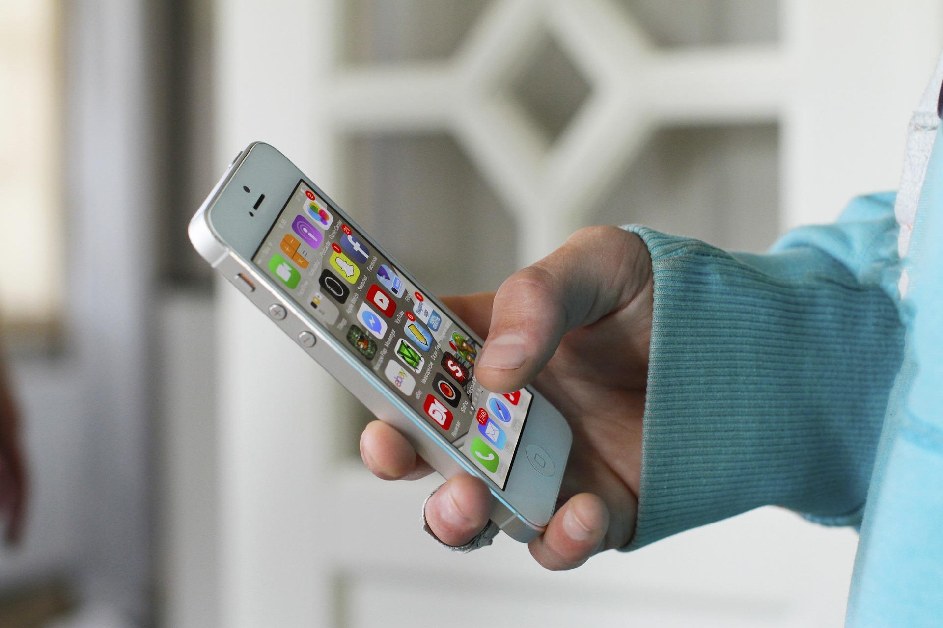 ręka trzymająca telefon, niebieska bluza, aplikacje na ekranie telefonu