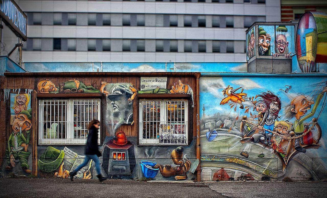 grafitti na ścianie, idąca kobieta w czarnej kurtce, w tle okna budynku