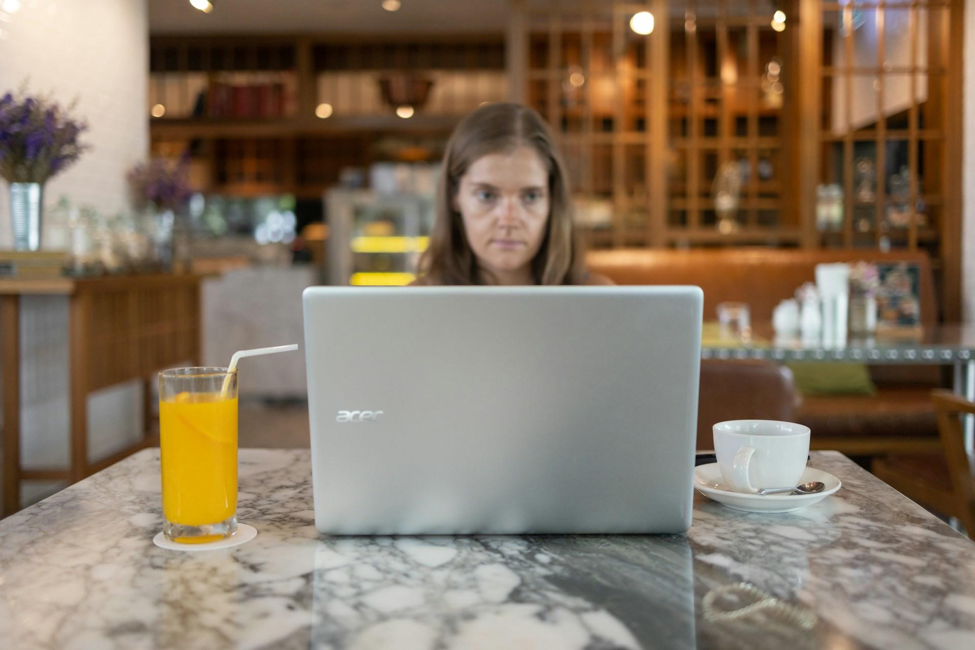 Kobieta przy komputerze, laptop na stole, filiżanka, sok pomarańczowy w szklance, kuchnia.