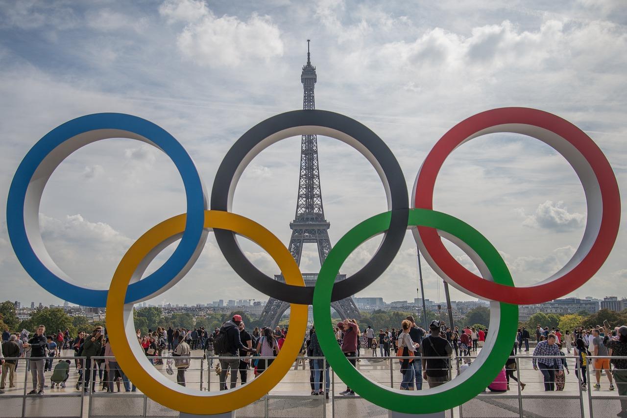 Symbol igrzysk olimpijskich, składający się z pięciu kolorowych pierścieni na tle Wieży Eiffla