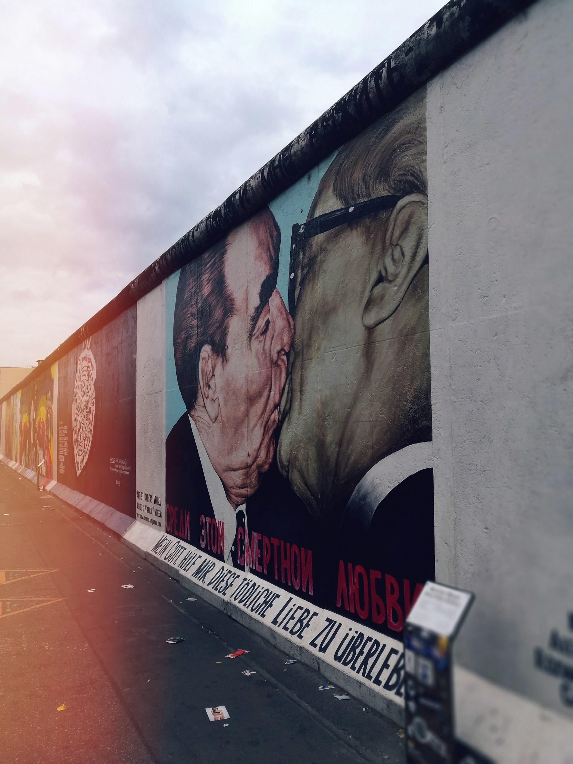 mur berliński, grafitti dwóch całujących się mężczyzn, promienie słońca po lewej stronie obrazka
