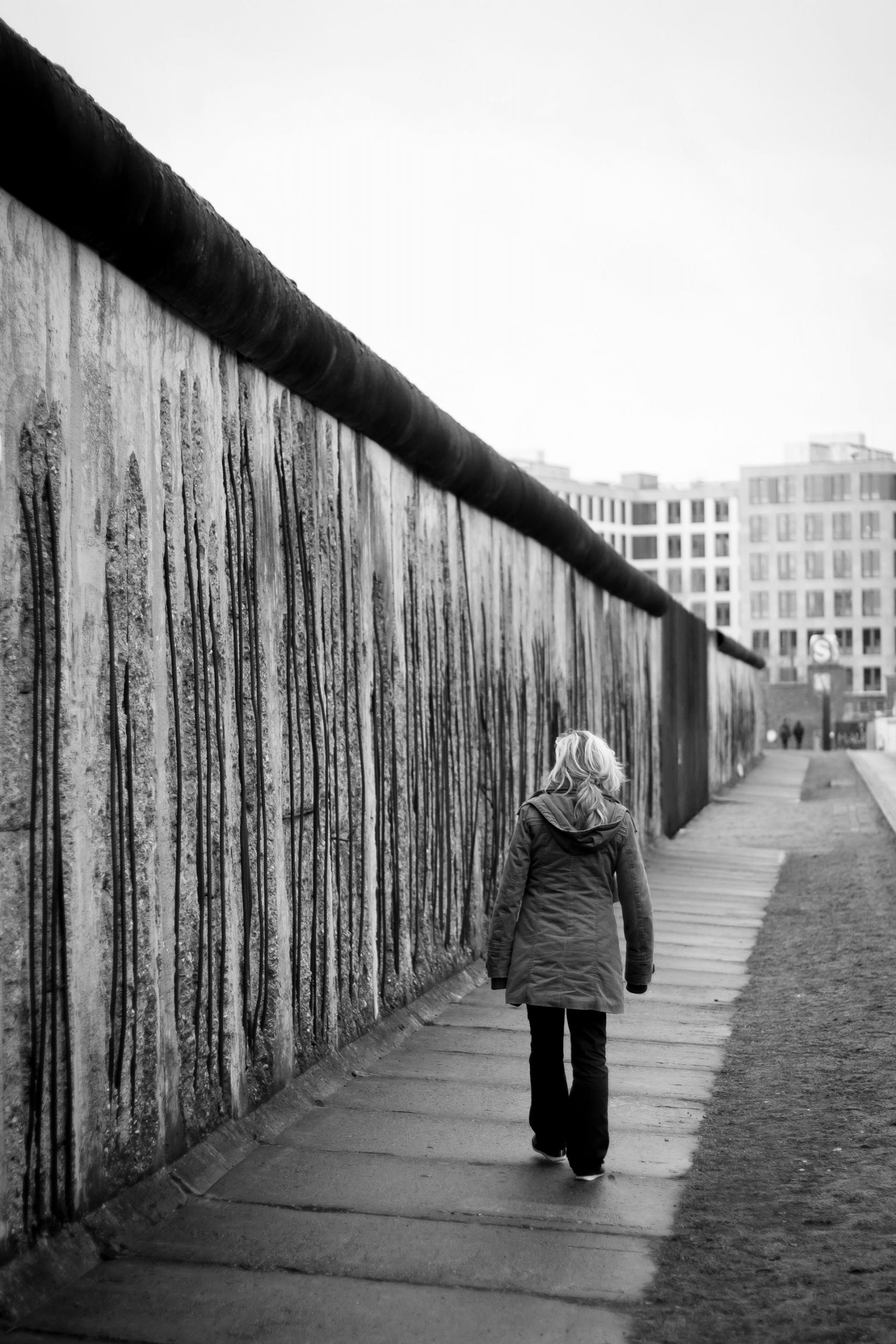 mur, kobieta idąca wzdłuż muru, czarno  białe zdjecie