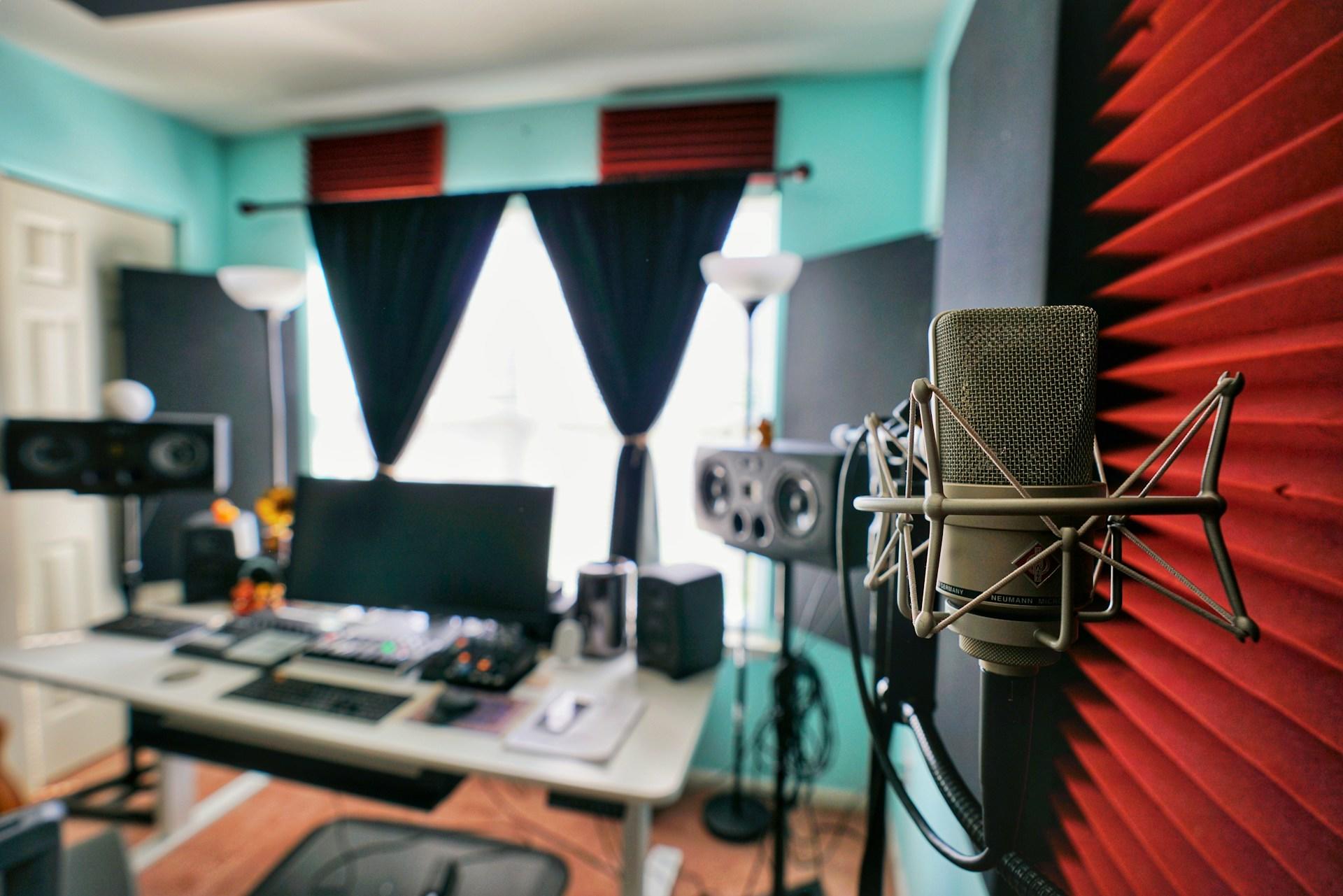 Studio dźwiękowe, mikrofon, biurko, komputer, okno, wygłuszenie pomieszczenia, nagrywanie dźwięku.