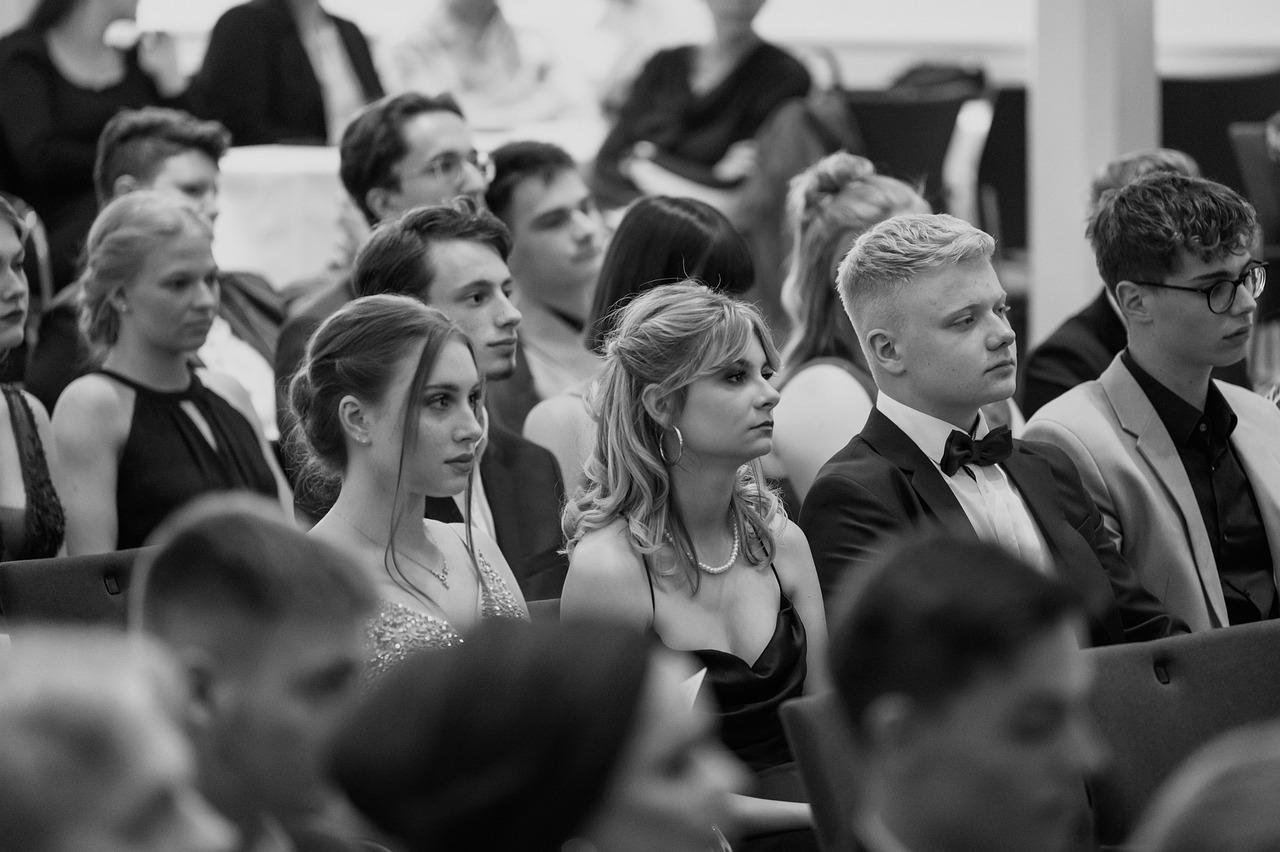 Uczniowie w eleganckich strojach siedzący i patrzący w jednym kierunku