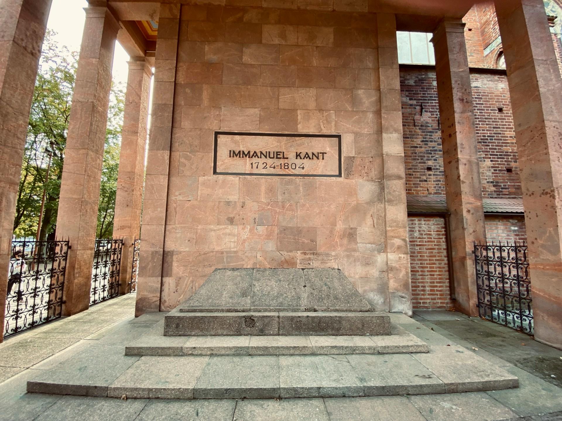 Grobowiec z czerwonej cegły z plakietką z napisem "Immanuel Kant" i betonowy nagrobek.