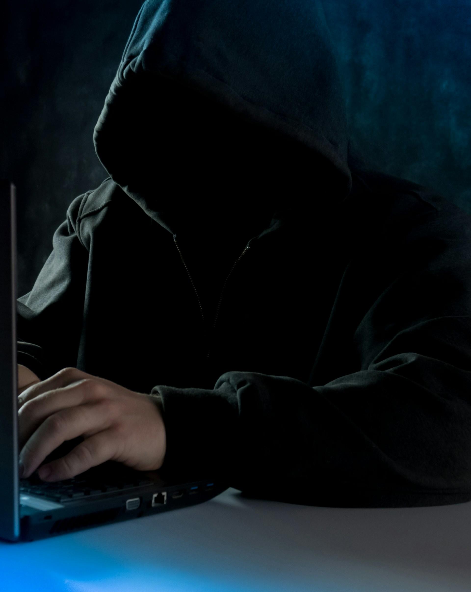 Mężczyzna z czarnym kapturem na głowie przy laptopie.