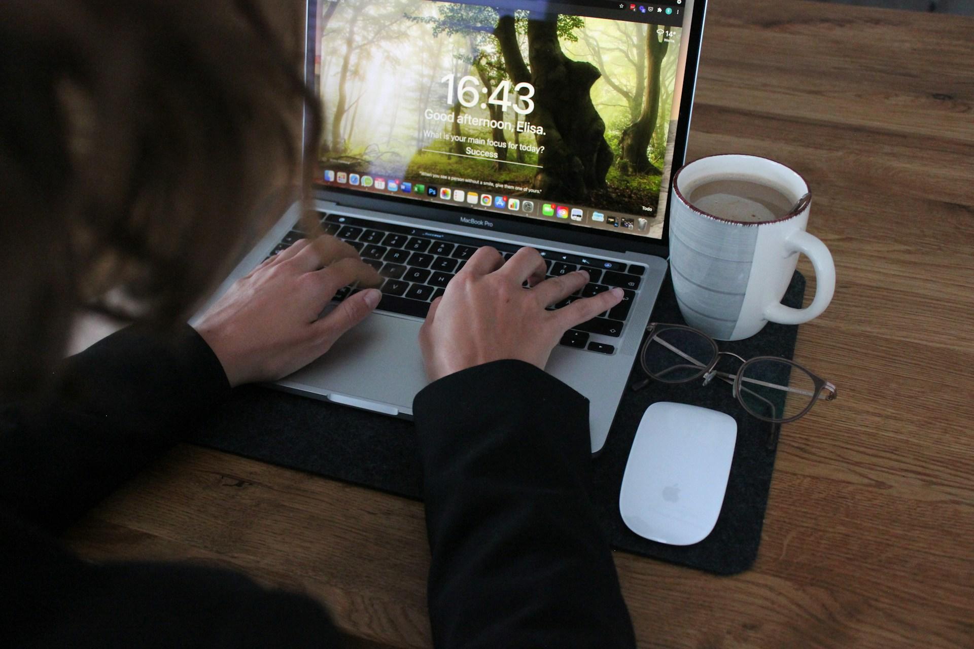 Osoba z dłońmi na laptopie przy biurku z kubkiem kawy.