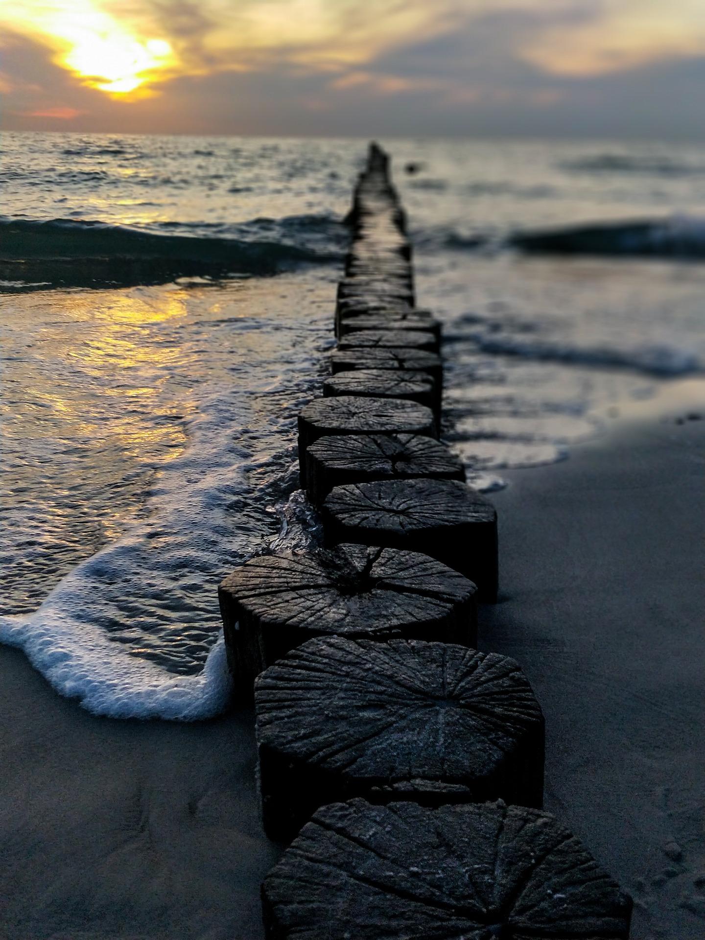Falochron, fale rozbijające się o drewniane kołki na plaży.