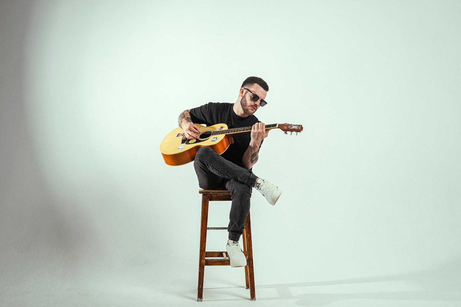 Mężczyzna z gitarą ubrany na czarno siedzący na krześle.