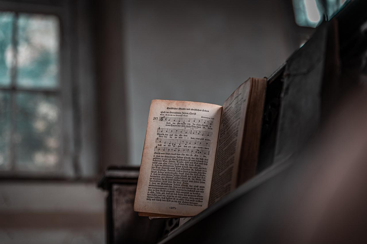 otwarta z nutami stara książka na pianinie, w tle ściana oraz okno