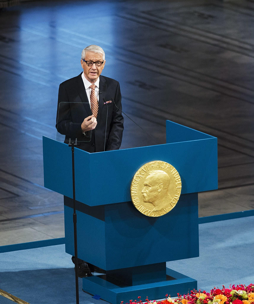 Ceremonia rozdania Nagrody Nobla, mężczyzna na niebieskim podium.