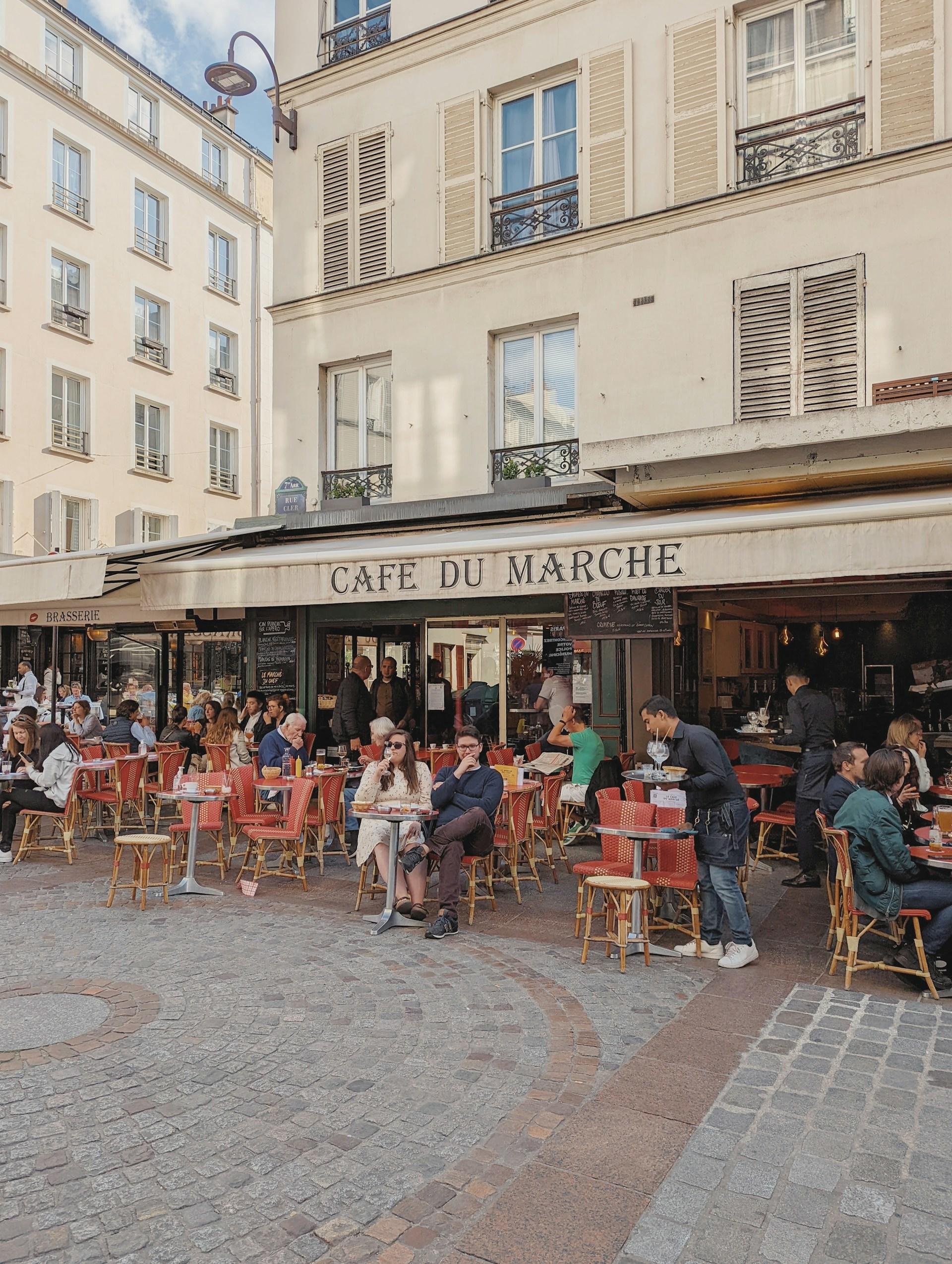 Ludzie przy stolikach kawiarnianych na zewnątrz budynku.