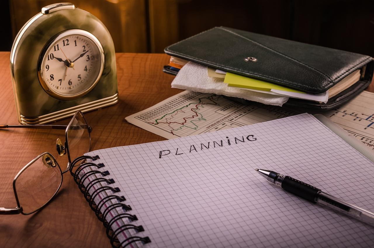 na biurku zeszyt z zapisem ''planning'', długopis oraz zegarek
