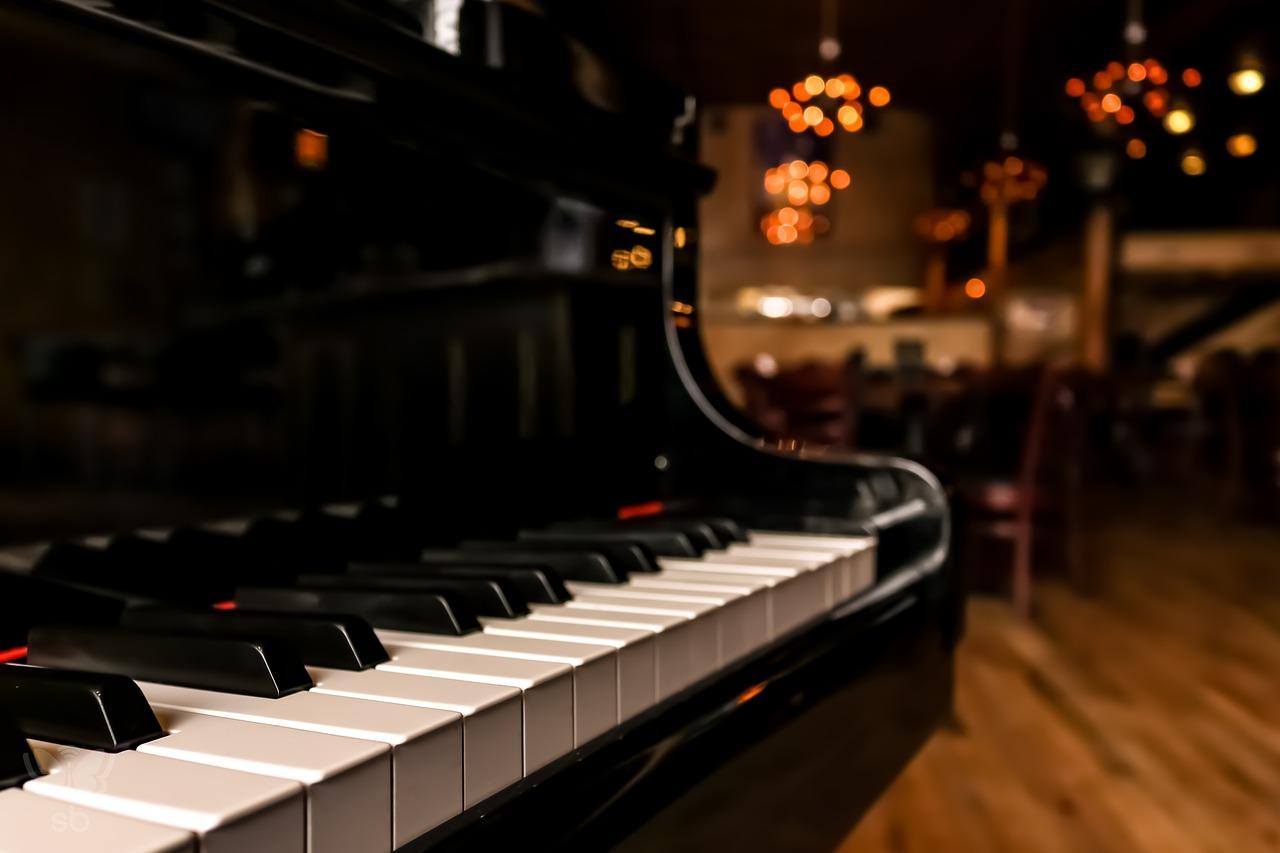 pianino na pierwszym planie, w tle światła i drewniana podłoga