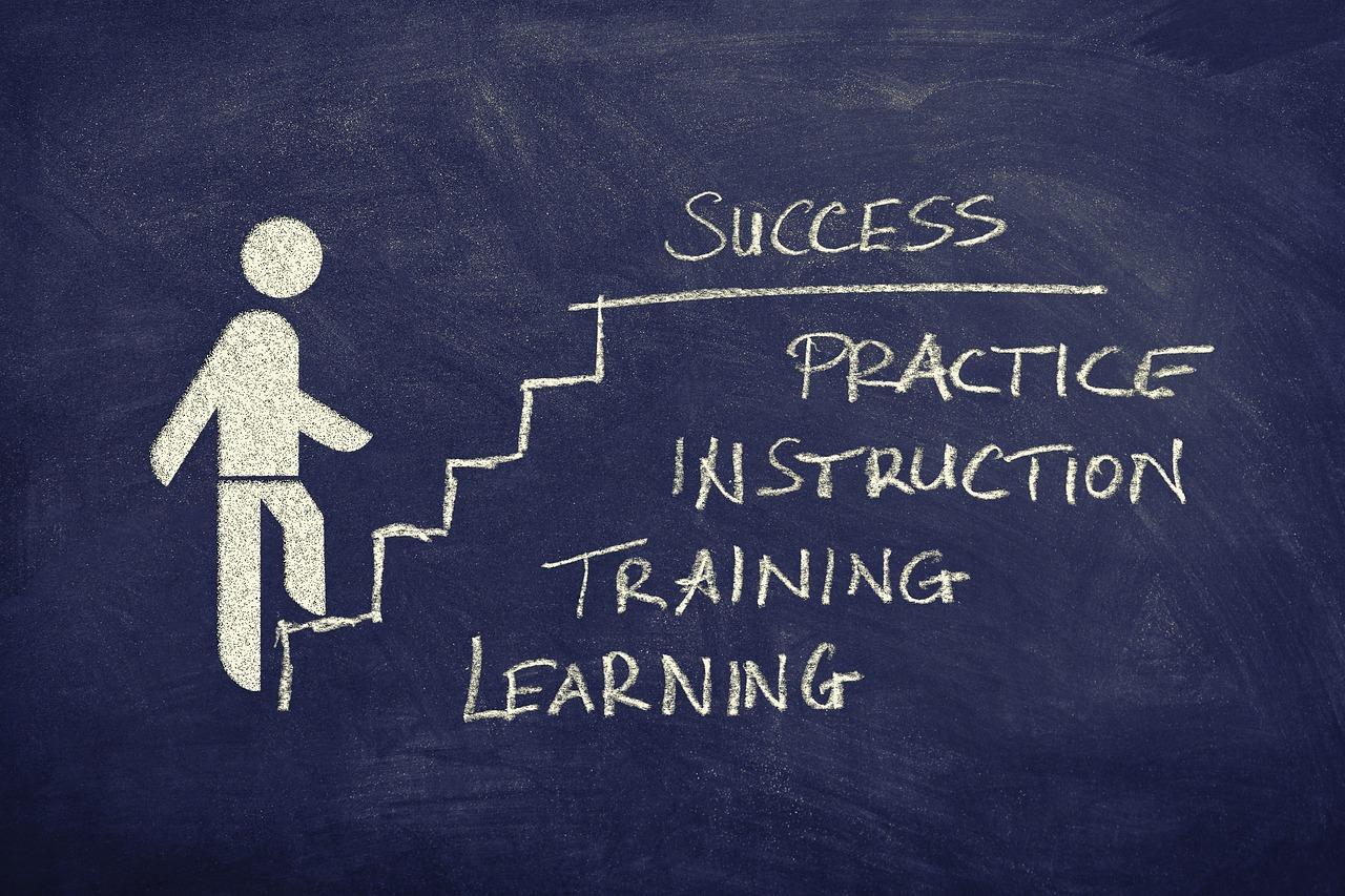 na tablicy narysowany człowieczek wspinający się po schodach i kolejno napisy: learning, training, instruction, practice i success