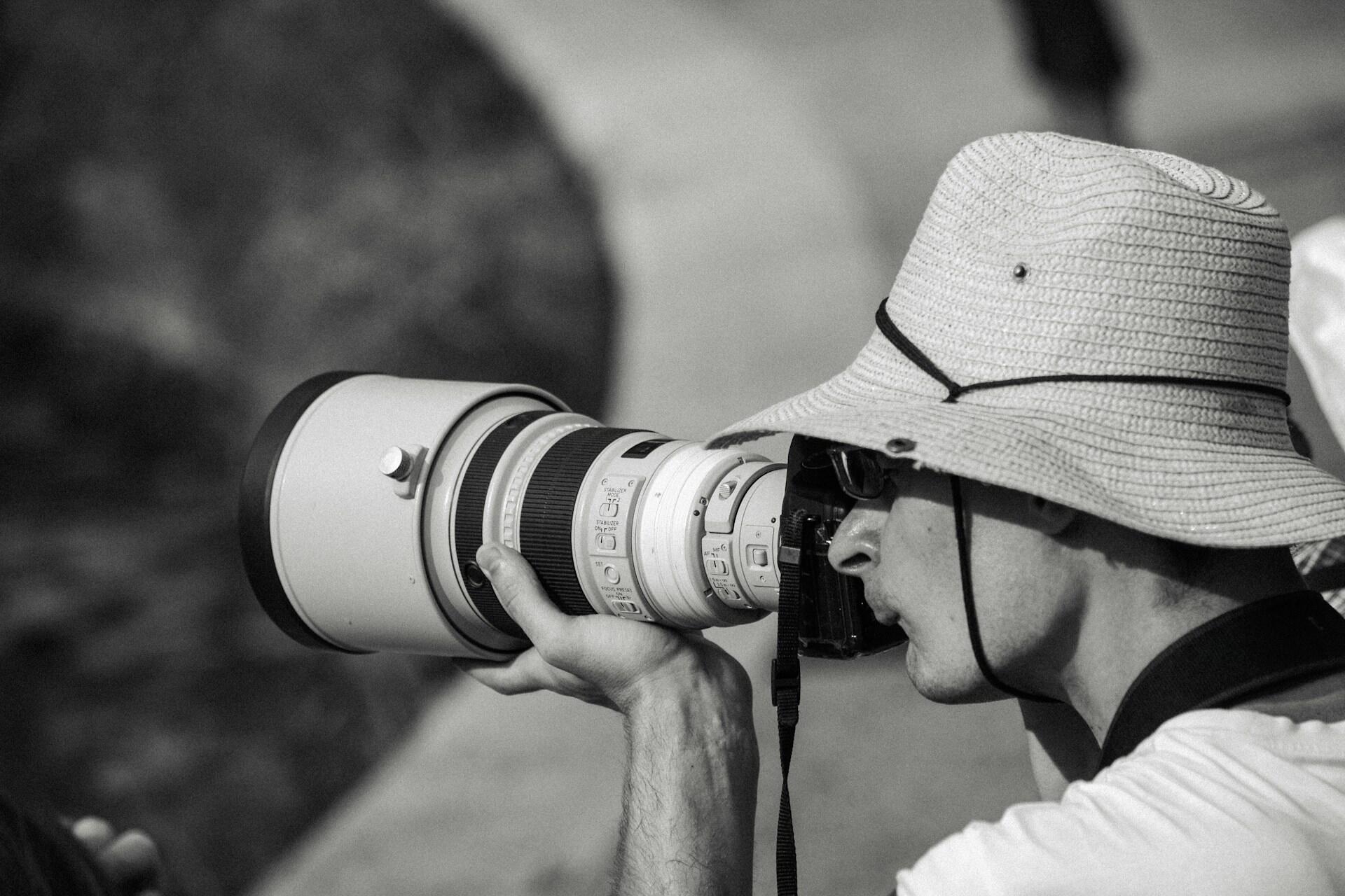 Fotograf w kapeluszu z aparatem fotograficznym o długim obiektywie.