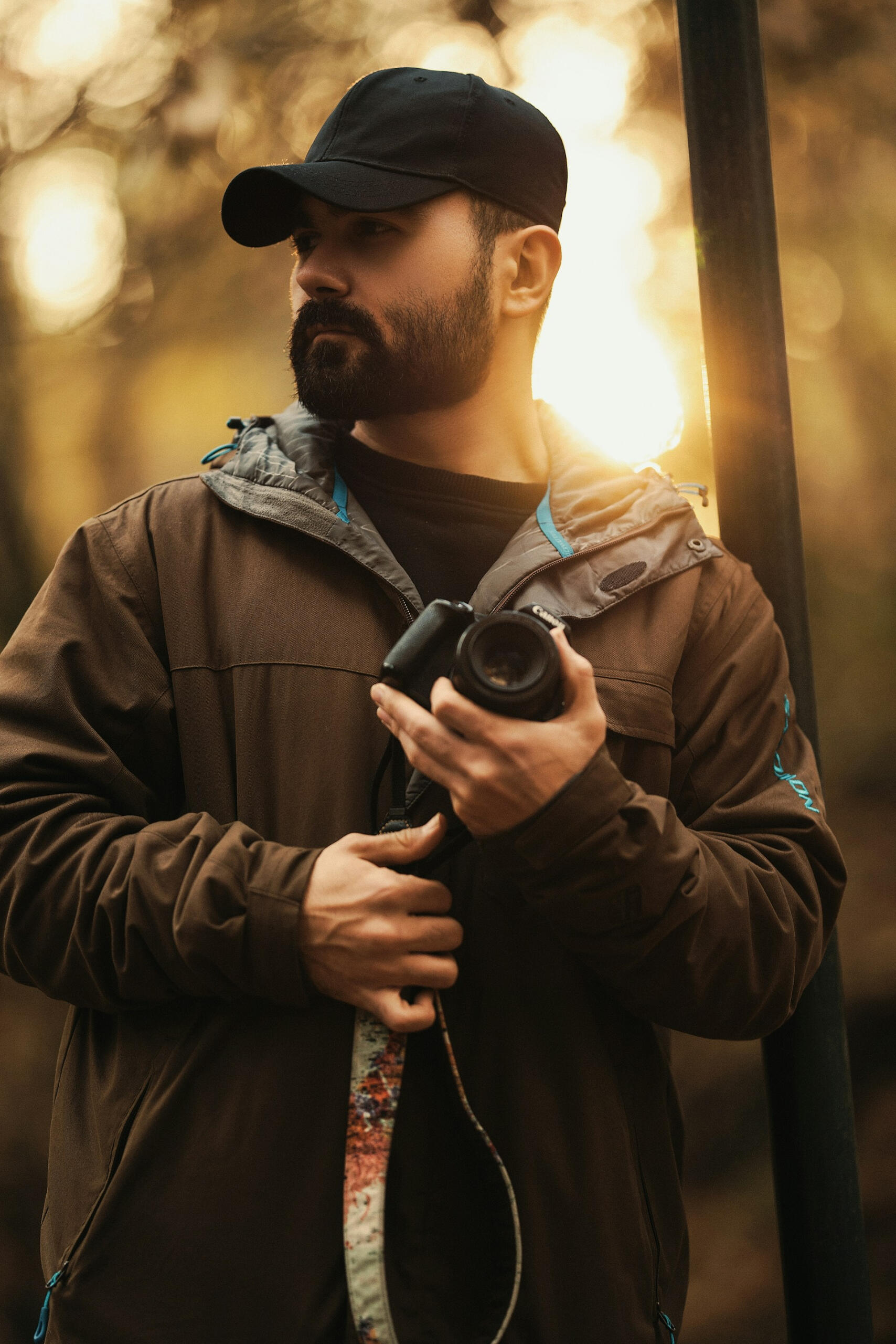 Brodaty mężczyzna z aparatem fotograficznym wśród drzew.
