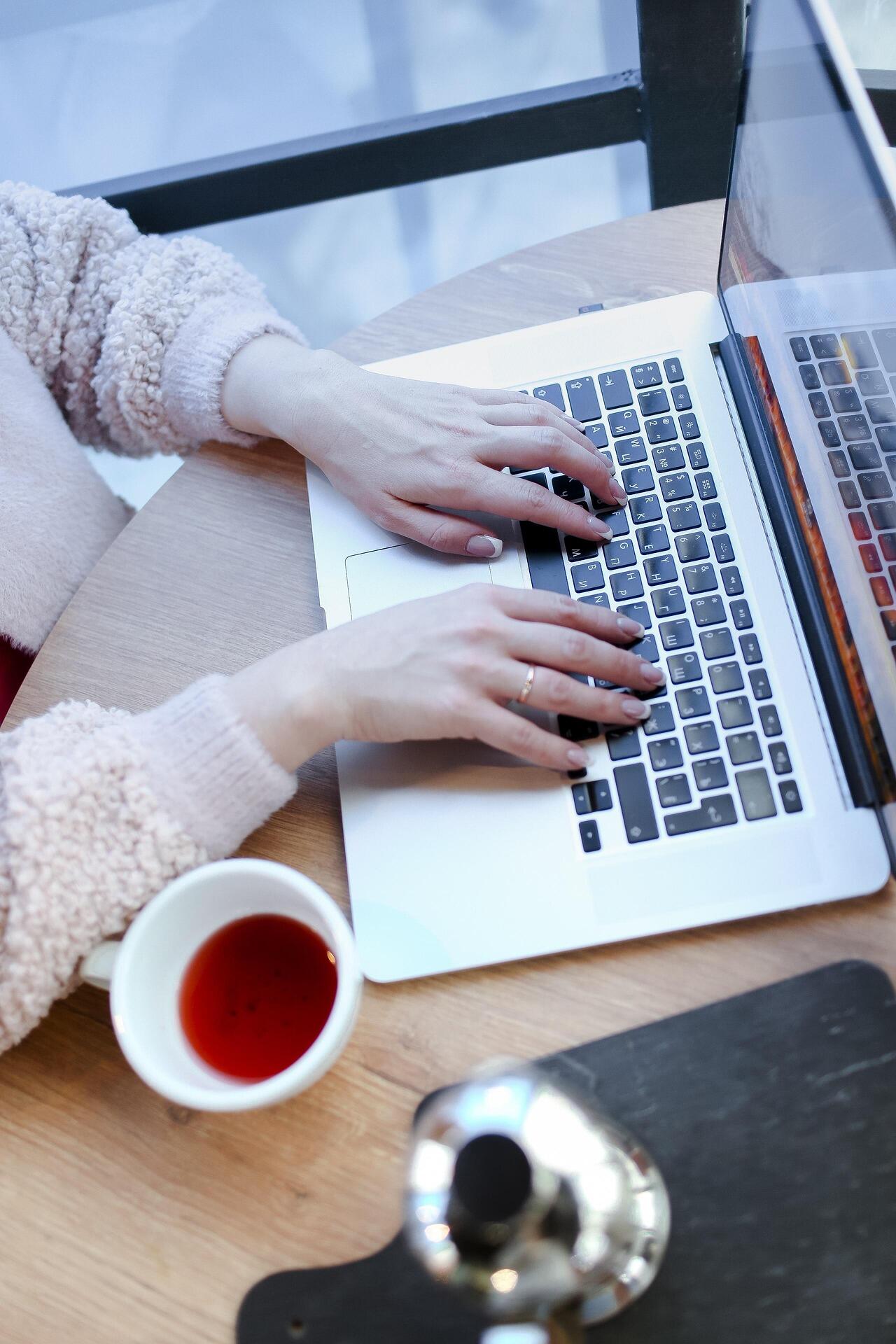 Kobiece dłonie na klawiaturze laptopa i herbata.