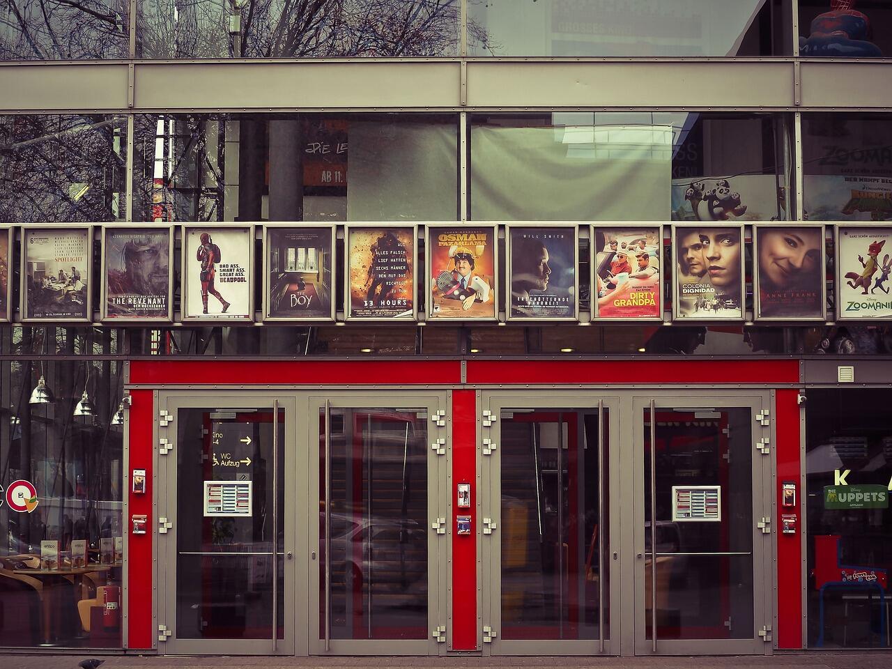 zdjęcie wejścia do kina, szklane drzwi, plakaty z filmami powieszone nad wejściem