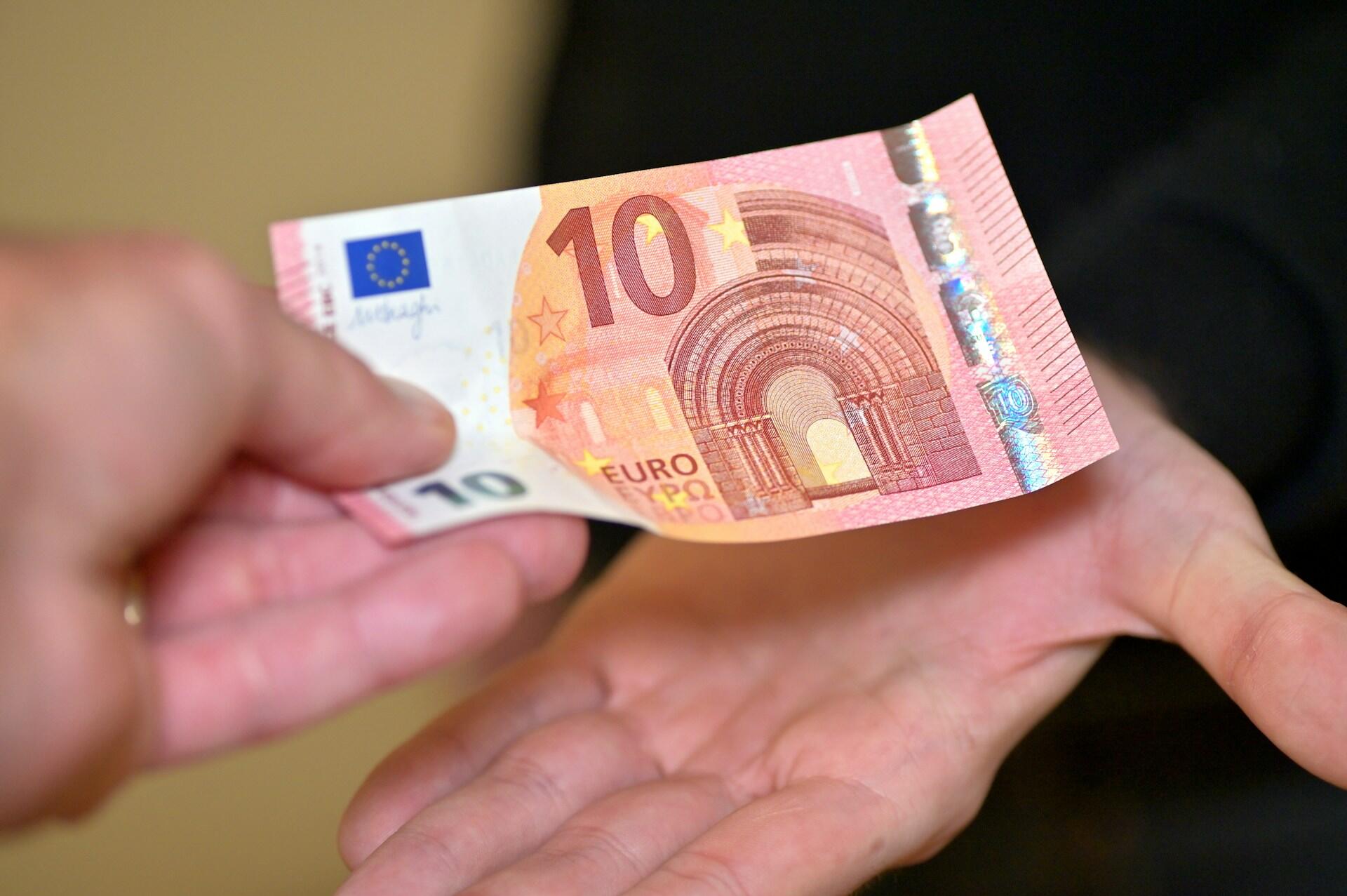 Dłoń przekazująca banknot drugiej dłoni.