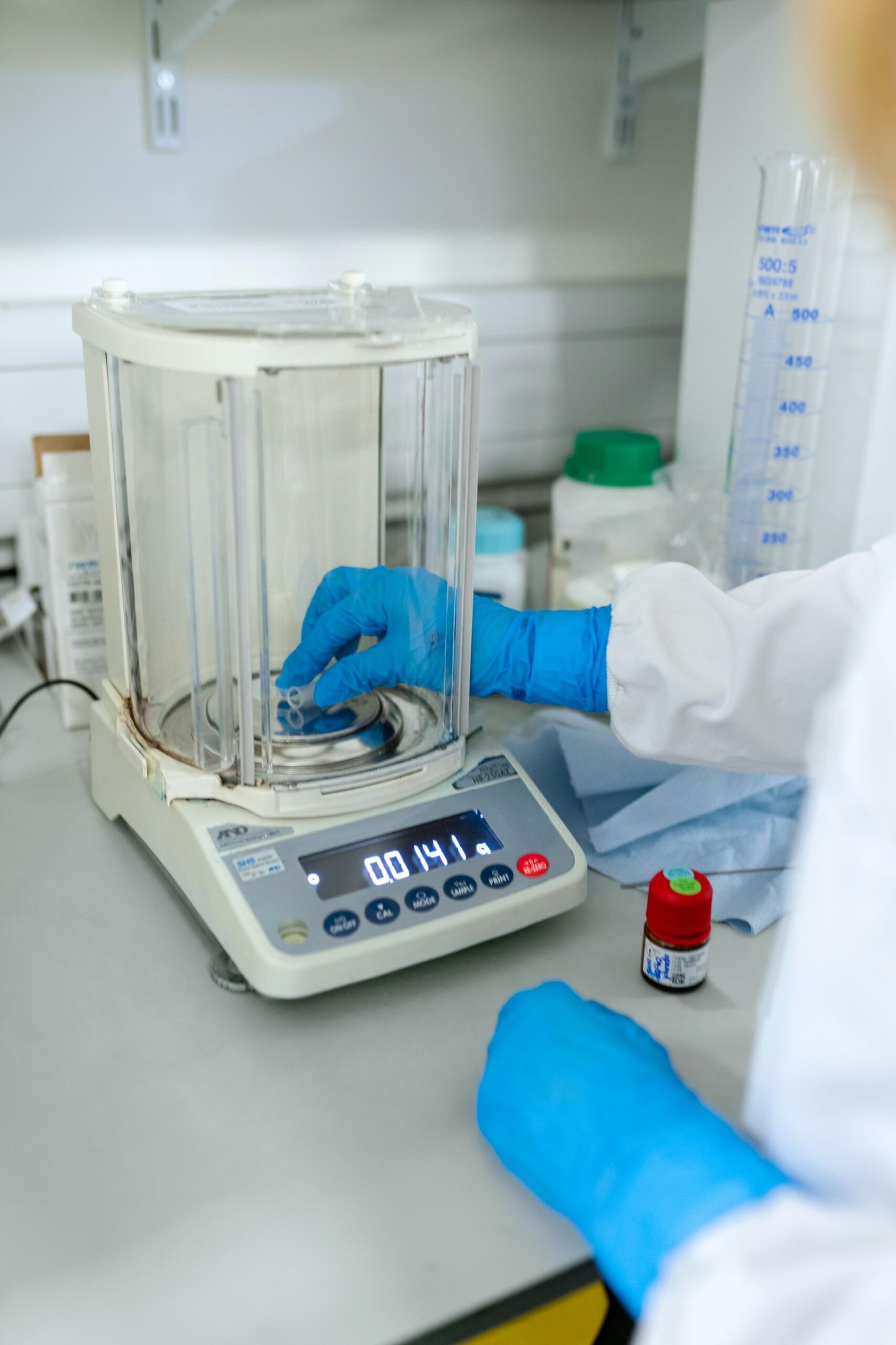 Chemik w niebieskich rękawiczkach ważący próbówkę.
