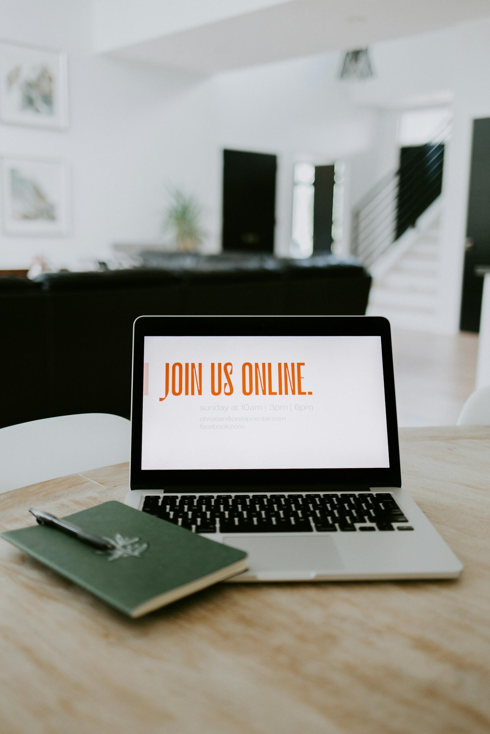 Otwarty laptop z napisem „join us online” i zeszyt na stoliku w salonie.