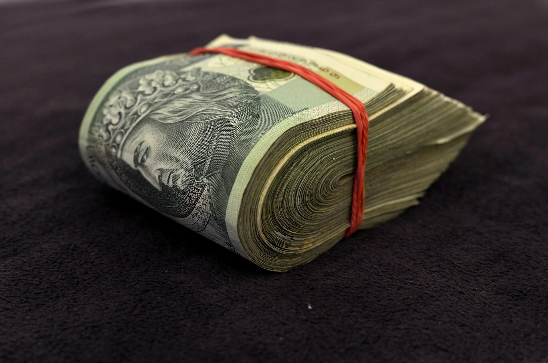 Plik banknotów stuzłotowych owinięty czerwoną gumką.