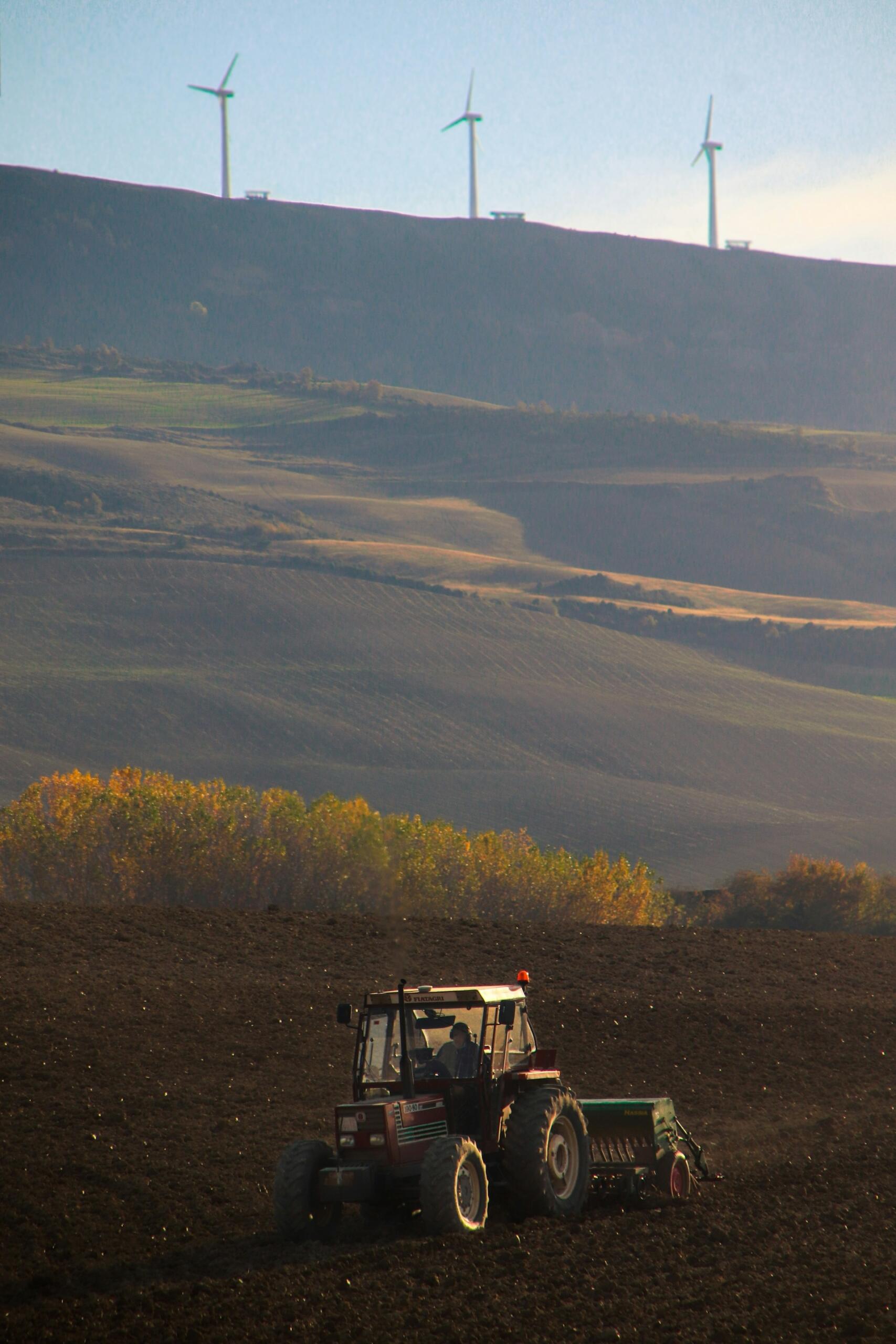Traktor na polu z wiatrakami energetycznymi na szczycie wzgórza.