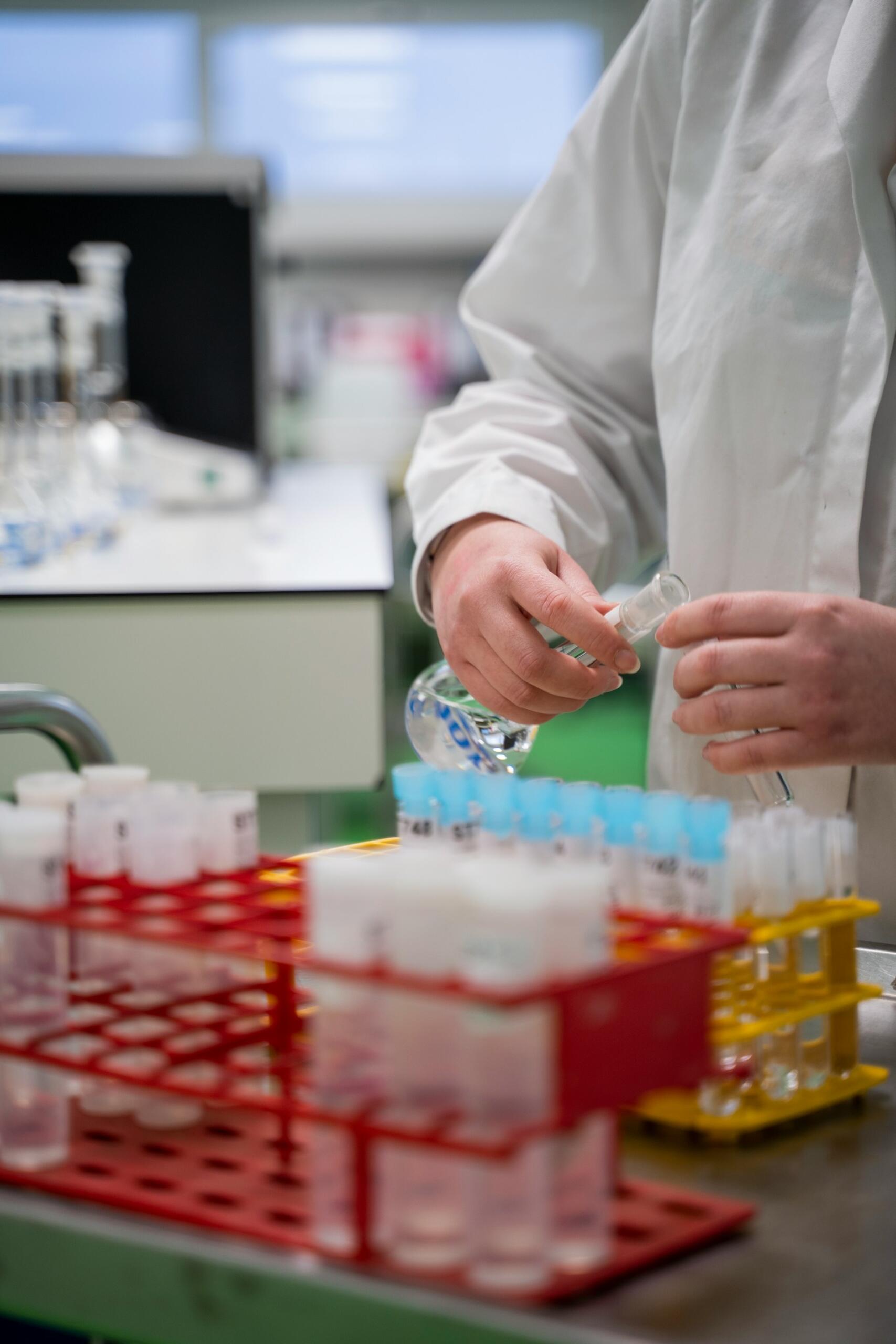 Chemik przelewający płyn z butelki do próbówki w laboratorium.